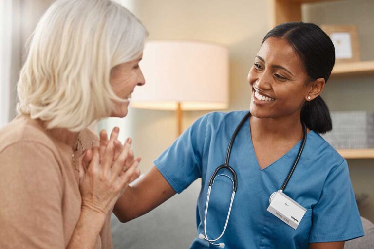 A senior resident in a cozy common area, chatting with a friend while staff nearby assists another resident.