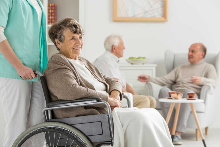 Caregiver calmly speaking with an older adult in a bright, uncluttered assisted living room.